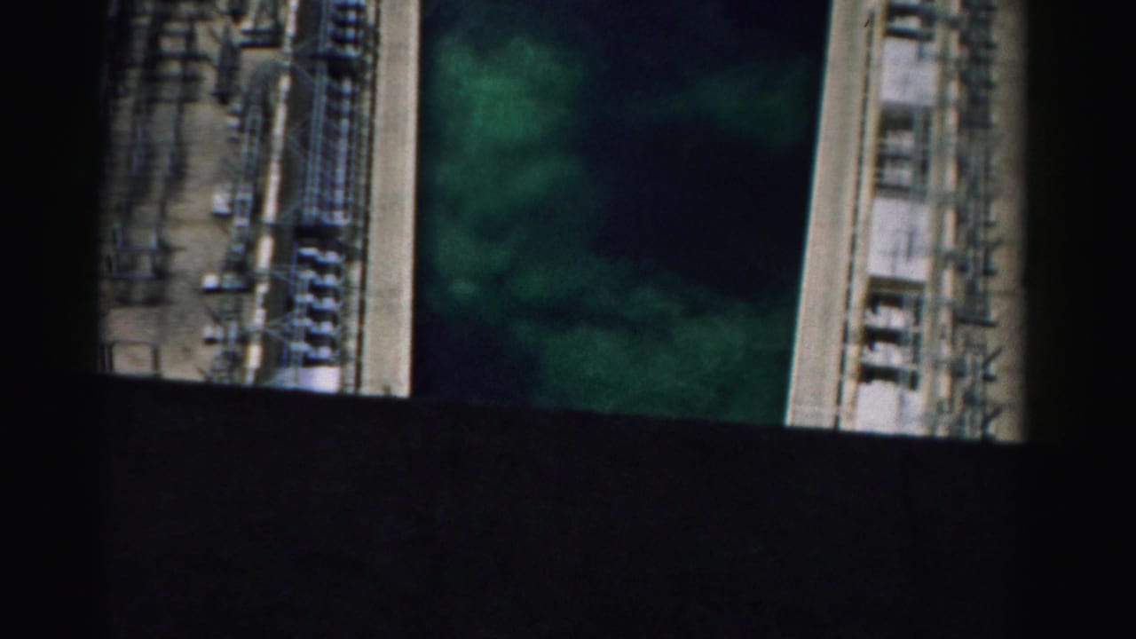 High-angle view of industrial equipment beside green water, partly obscured by black frame bands.