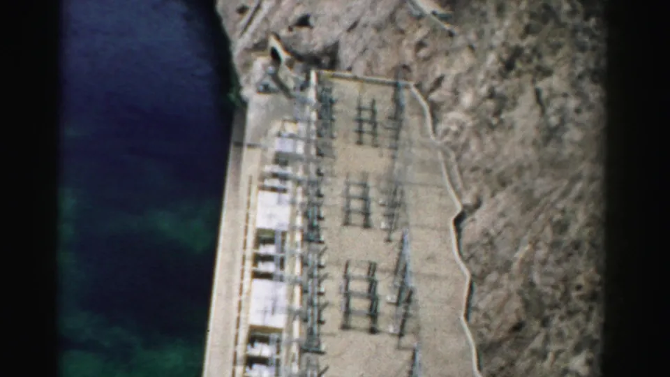 1957 Nevada 8mm frame showing water, concrete infrastructure, electrical equipment, and rocky canyon terrain from above.