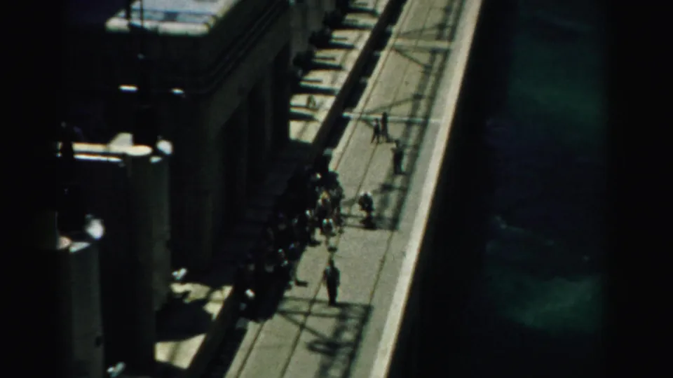 High-angle 1950s Nevada view of tourists moving along an elevated dam walkway beside concrete forms and water.