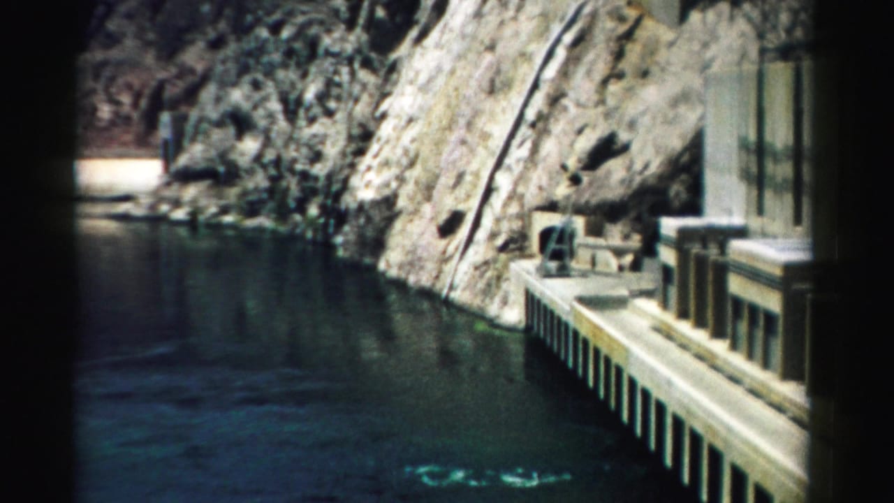 1957 Nevada home-movie frame showing a concrete dam platform against canyon rock and dark green water.
