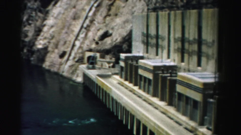 1957 Nevada 8mm frame with concrete dam face, platform edges, and canyon water below steep rock.