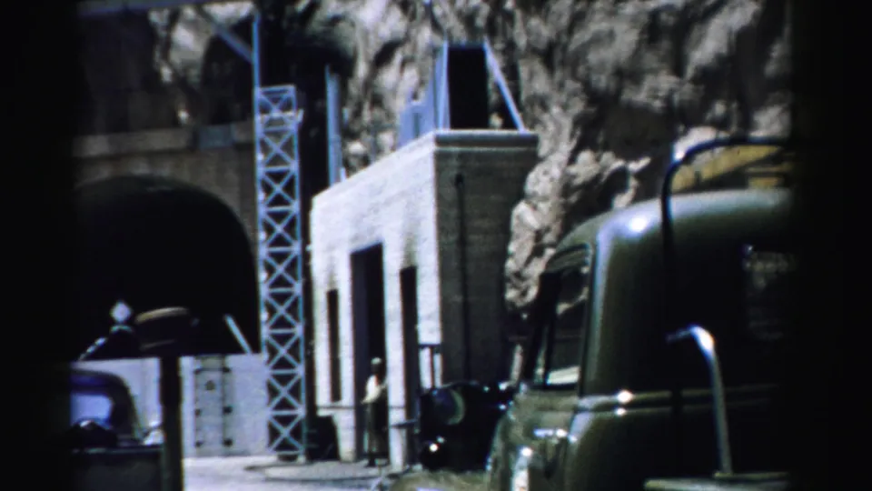 1957 Nevada 8mm frame showing a tunnel portal, temporary building, vehicles, and small figures at a rocky construction site.