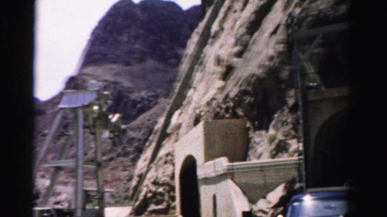 Mountain slope with a metal shaft structure, concrete wall, tunnel edge, and partial vehicle at right.