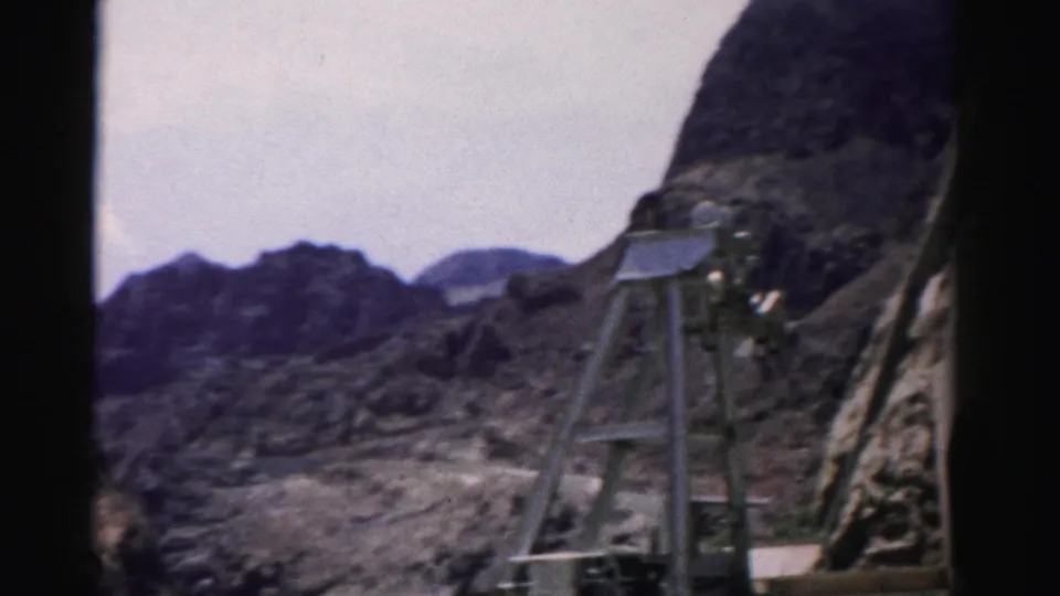 1957 Nevada 8mm frame showing an arid rocky landscape with a metal shaft structure below dark mountain ridges.