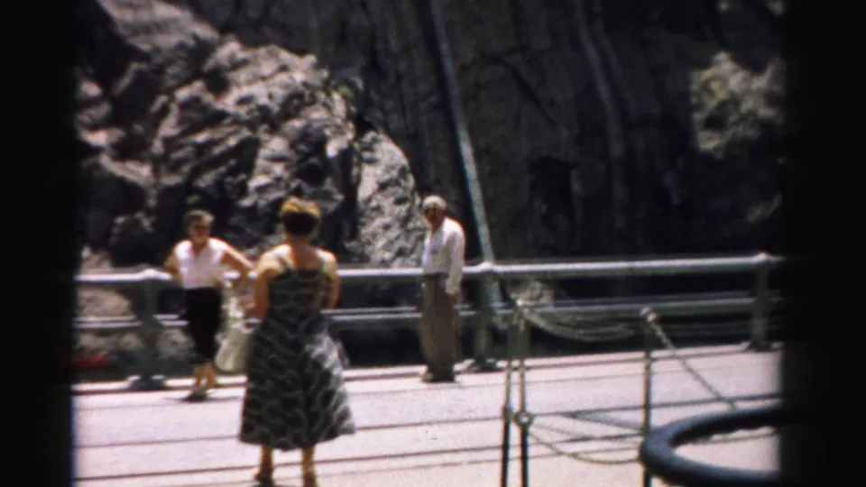 A small group of visitors stands near metal guardrails and a dark tunnel or passage opening in the rocky Nevada pass.