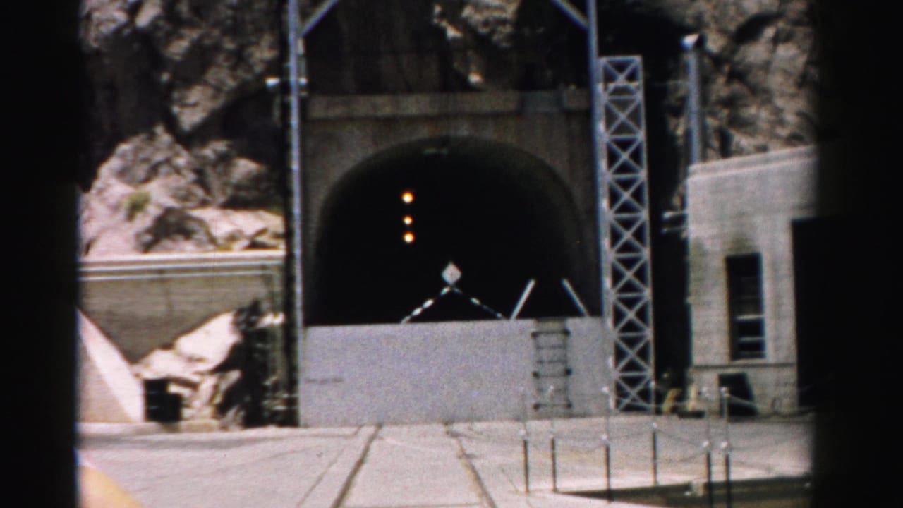 Concrete tunnel entrance set into rocky cliffs with barriers in front.