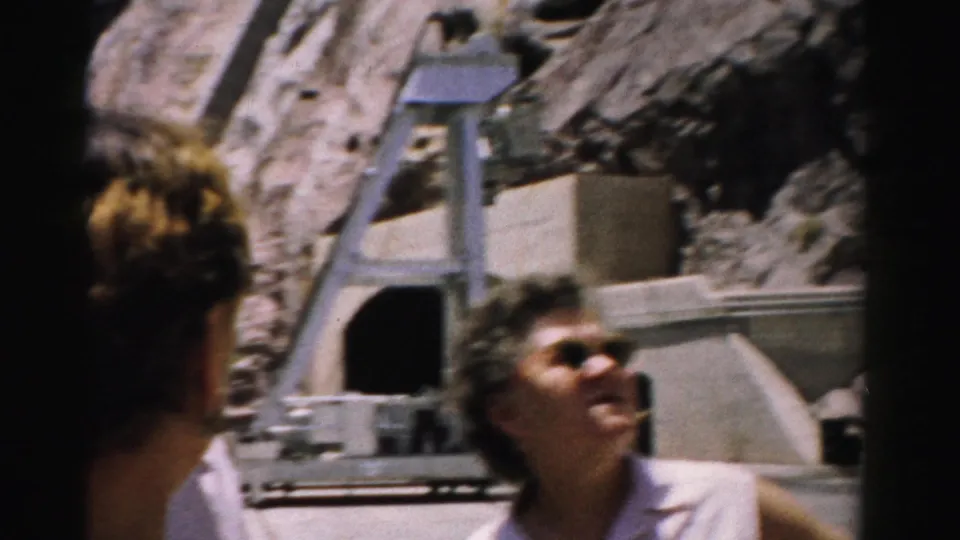 Two women, one partly turned away and one in sunglasses, stand near a concrete tunnel structure in a rocky Nevada canyon setting.