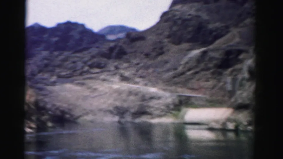 Soft 8mm view of reservoir water, pale shoreline, and rugged Nevada canyon hills from a handheld visitor perspective.