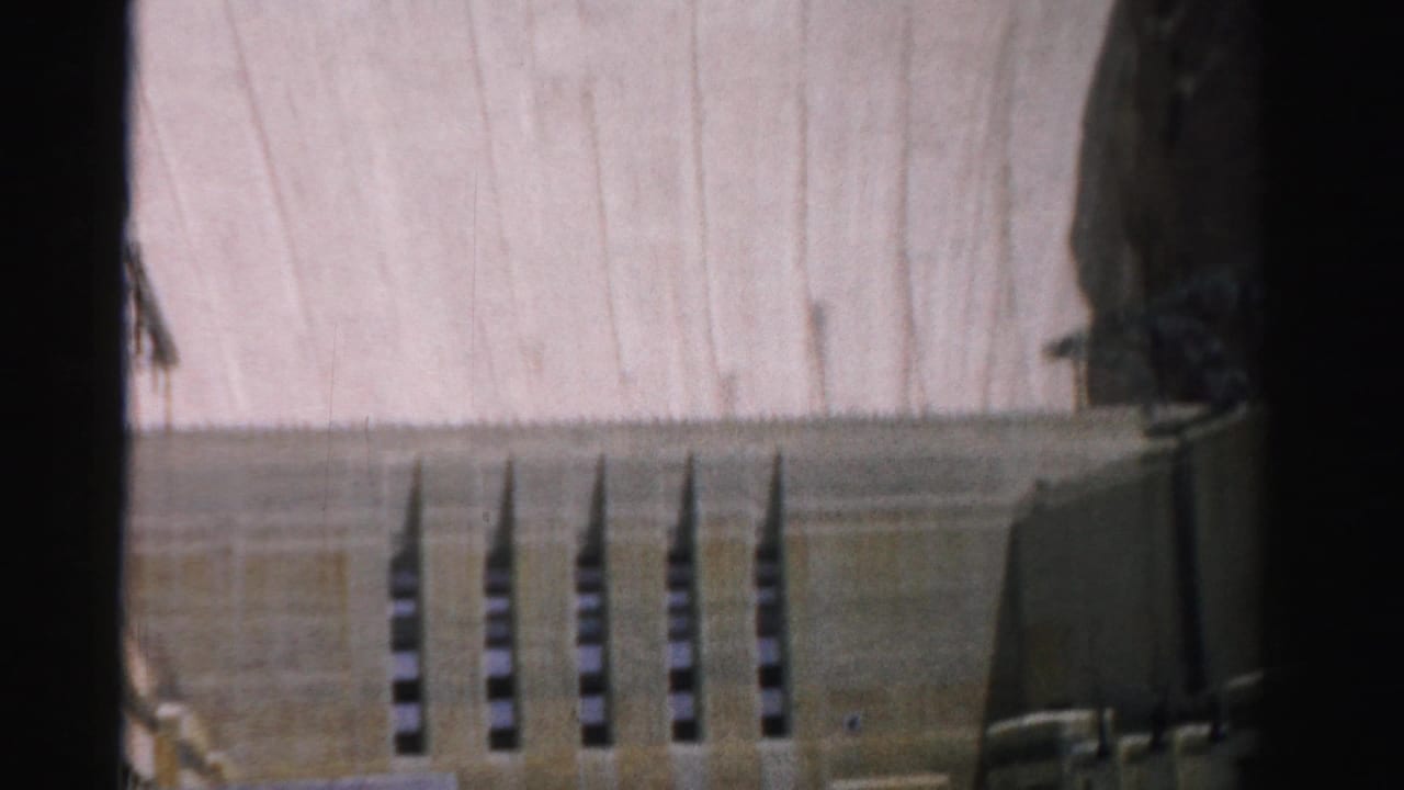 Concrete dam face with vertical openings and canyon edges.