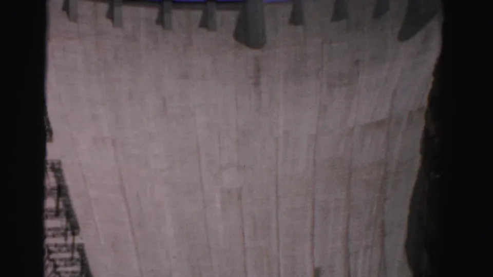 1957 8mm low-angle view of Hoover Dam's tall concrete wall rising between shadowed canyon sides.