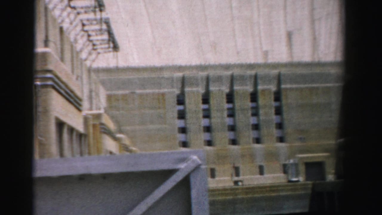 1957 Nevada 8mm frame showing a beige concrete industrial structure with vertical vents and dark film-gate edges.