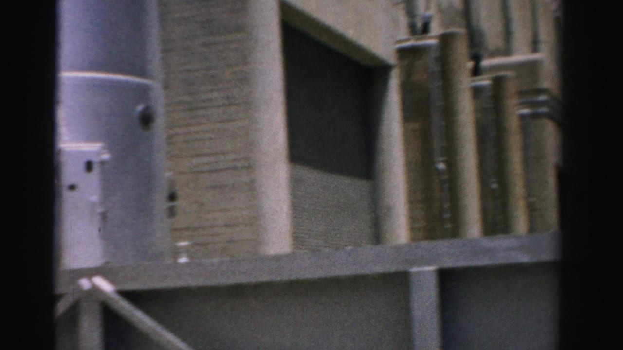 1957 Nevada 8mm view of a concrete industrial exterior with silver pipework, railing, and dark frame borders.