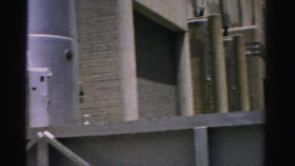 1957 Nevada 8mm view of a concrete industrial exterior with silver pipework, railing, and dark frame borders.