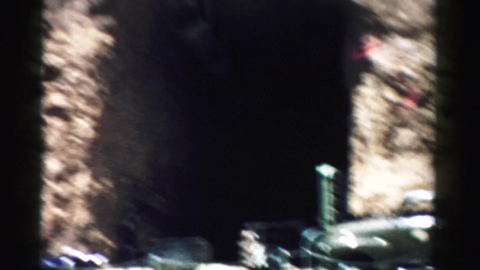 Soft 8mm frame from Nevada showing a green truck in motion blur near a dark opening and sunlit rock wall.
