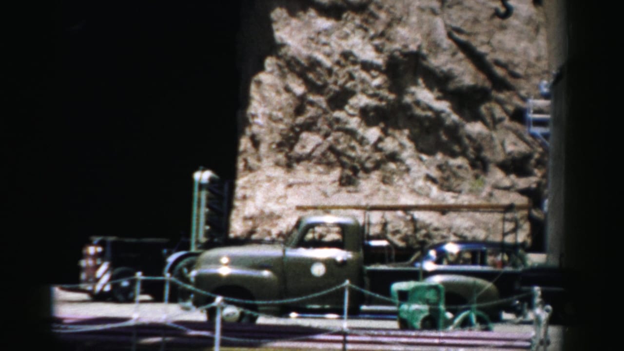 Vintage vehicle near a rocky roadside or dock area with railings and equipment in front.