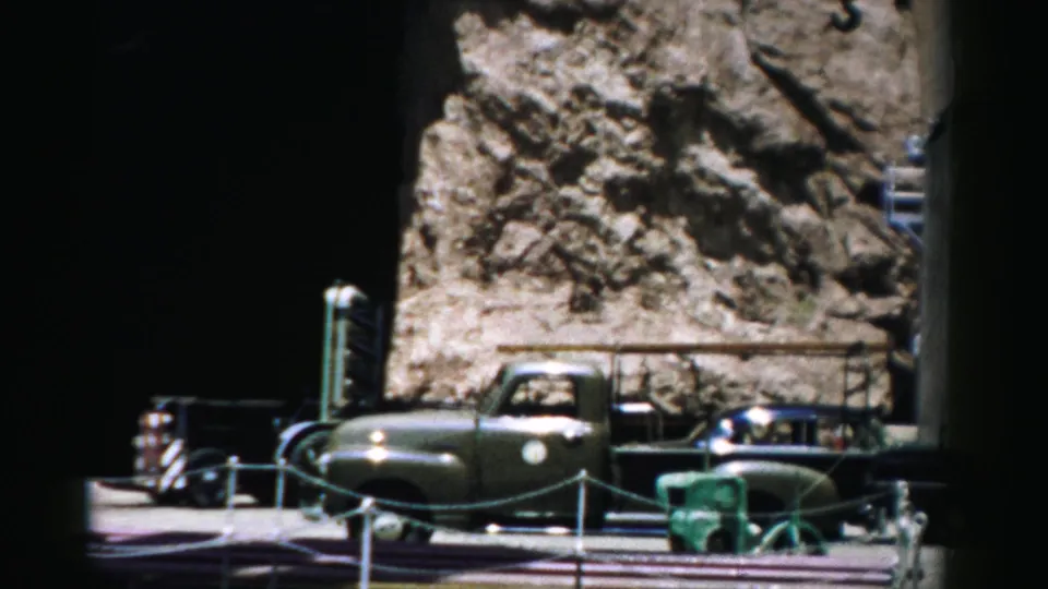 1957 Nevada 8mm frame showing a vehicle beside a rocky embankment, railings, and dockside or roadside equipment.