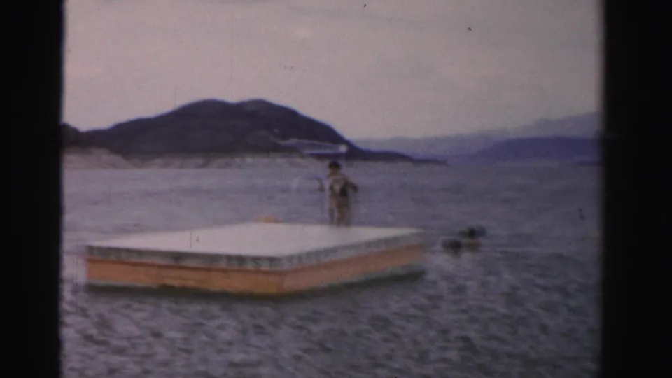 1957 Nevada lake scene with a floating platform, swimmers in the water, and low mountains visible across the hazy shoreline.