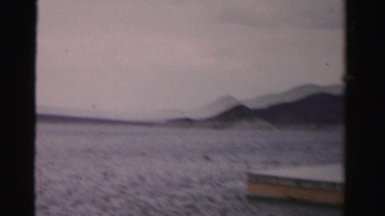 1957 Nevada home-movie frame showing open lake water, distant hills, and the edge of a floating swim platform at the right side of the frame.