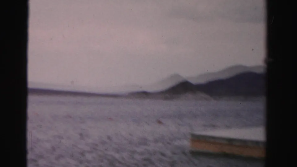 1957 Nevada home-movie frame showing open lake water, distant hills, and the edge of a floating swim platform at the right side of the frame.