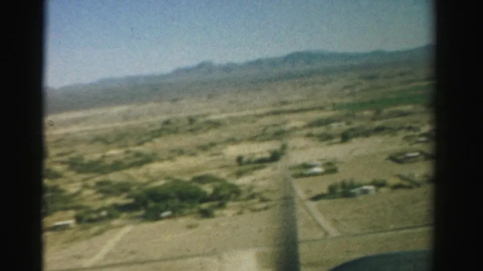 The final frame shifts to a soft, faded view of dry Nevada terrain with roads, scattered structures, and low hills in the distance.