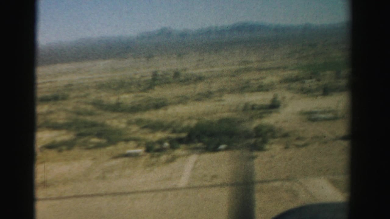 Aerial view through an airplane window over dry farmland and distant mountains.