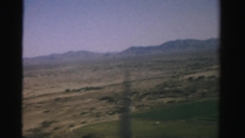 1957 Nevada desert terrain and low mountains viewed through a dark airplane window frame from a passenger seat.