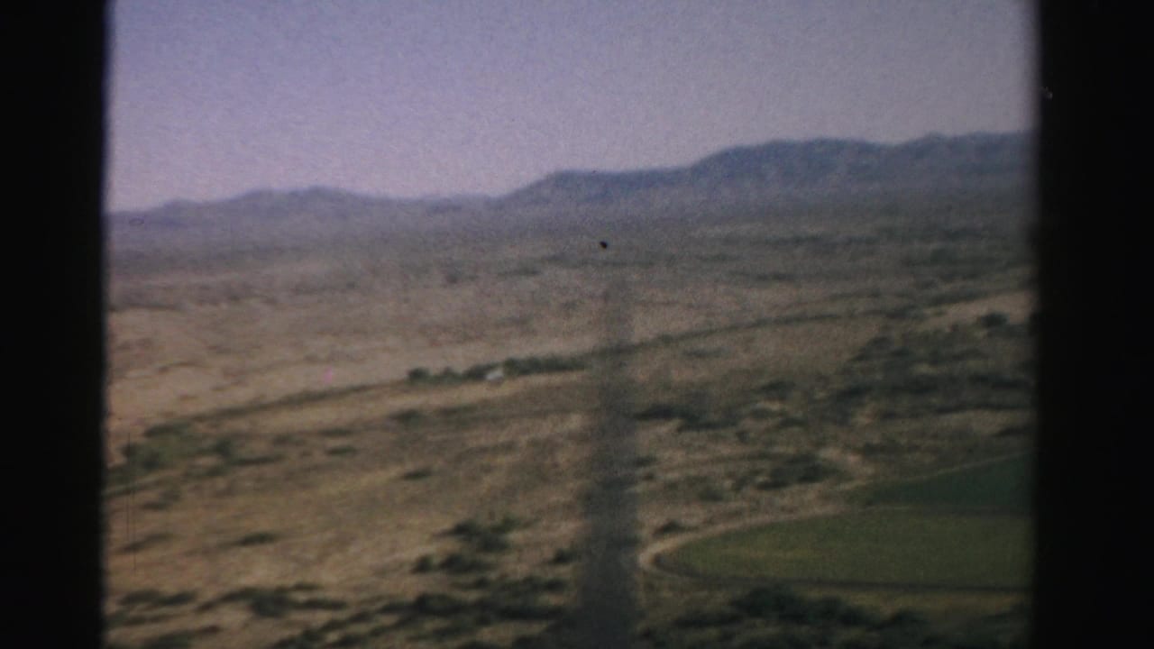 Aerial desert view through a divided airplane window with mountains beyond.