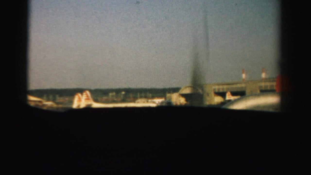Airliners and airport buildings viewed through adjacent airplane windows.