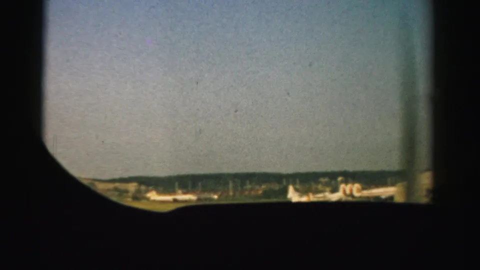 A passenger-window view over a Nevada airport tarmac, with small airliners partly visible below a hazy mid-century sky.