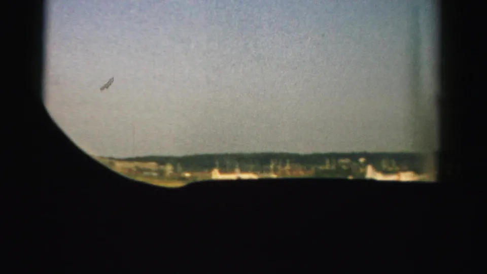 1957 Nevada home-movie frame with pale sky, distant ridge or tree line, and heavy dark viewfinder framing around the scene.