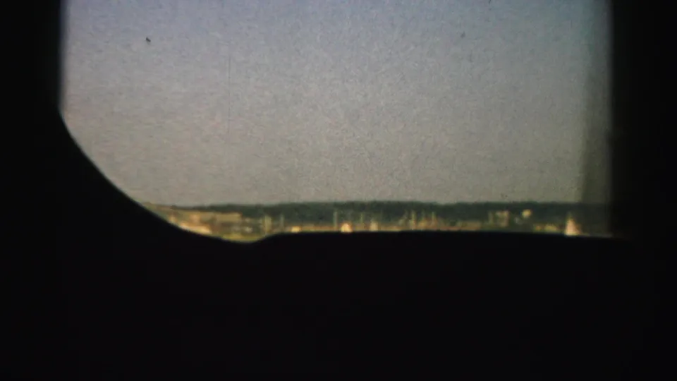 1957 Nevada 8mm frame showing a low distant horizon and pale sky, with a dark curved viewfinder-like edge covering much of the foreground.