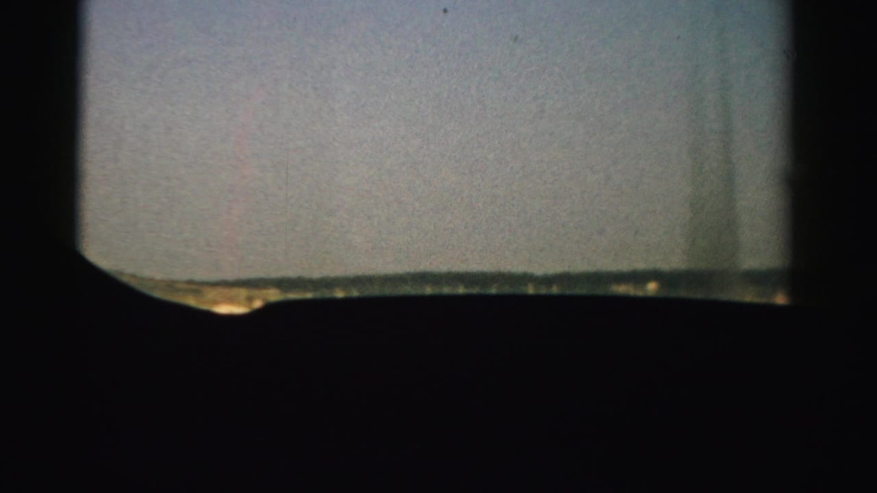 Airplane window silhouette framing pale sky and a low runway edge below.