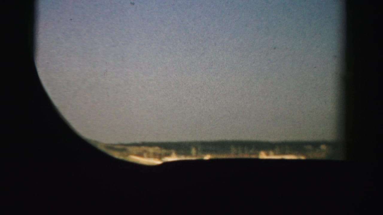 Curved airplane window view with runway and flat terrain along the lower edge.