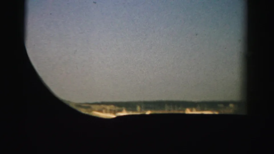 A dark aircraft window frames a sunlit runway and low Nevada landscape during the early takeoff view.