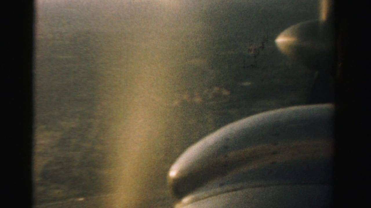 Small aircraft propeller and engine seen through a dark window frame above hazy terrain.