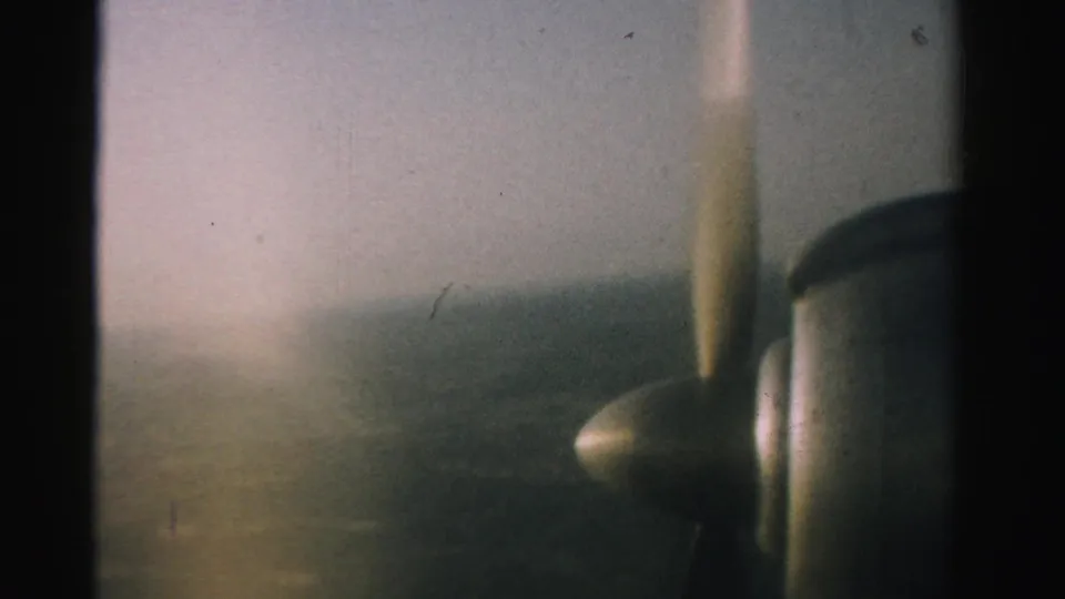 A soft 8mm aerial frame from the 1957 Nevada clip, with propeller blur and engine detail beside the horizon.