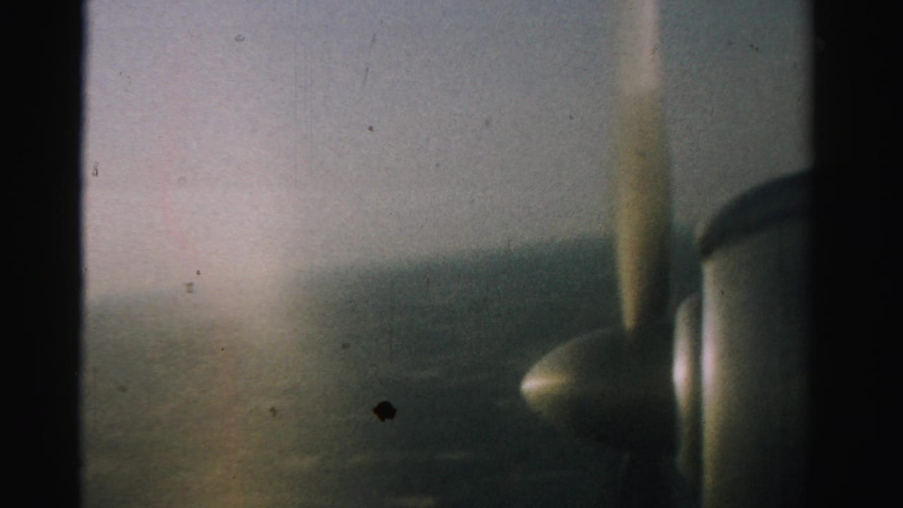 Hazy airplane window view with a blurred propeller at the right and distant ground below.