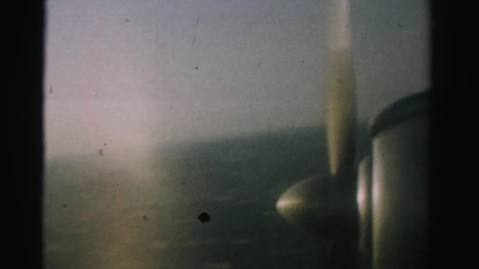 1957 Nevada 8mm frame showing a soft aerial view from an airplane window, with the spinning propeller blurred at right.