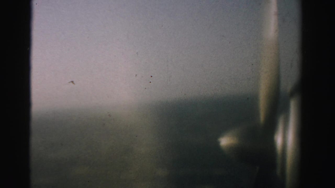 Airplane propeller and window edge dominate the right side over a muted aerial landscape.