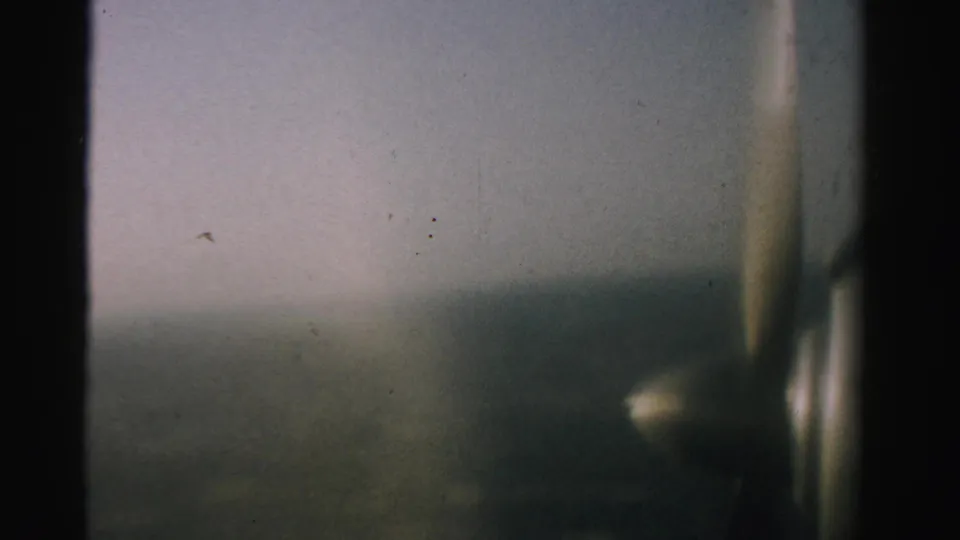 A 1957 Nevada passenger-window view shows a blurred propeller against pale sky and indistinct ground far below.