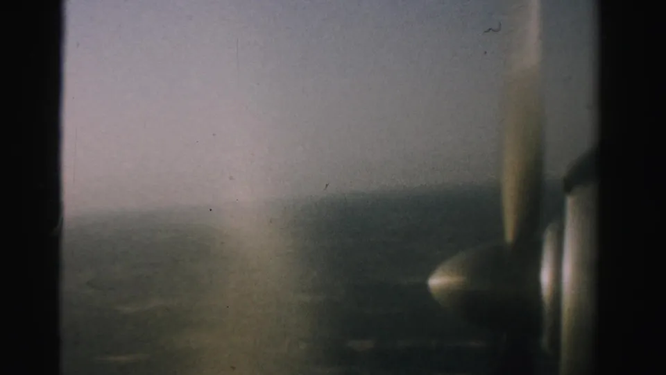 1957 Nevada 8mm footage frame with the aircraft propeller at right and a foggy or hazy landscape below.