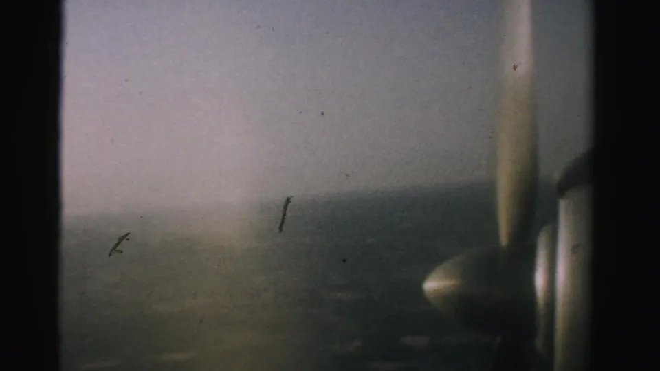 A final 1957 Nevada 8mm frame shows the propeller and aircraft window edge over a subdued aerial panorama.