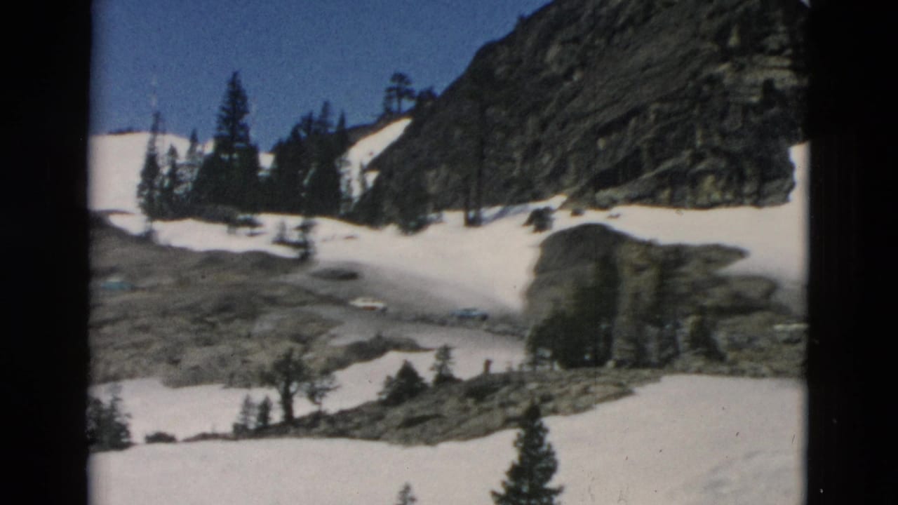 Snowy mountain basin with rocks, evergreens, and a dark vertical film edge.