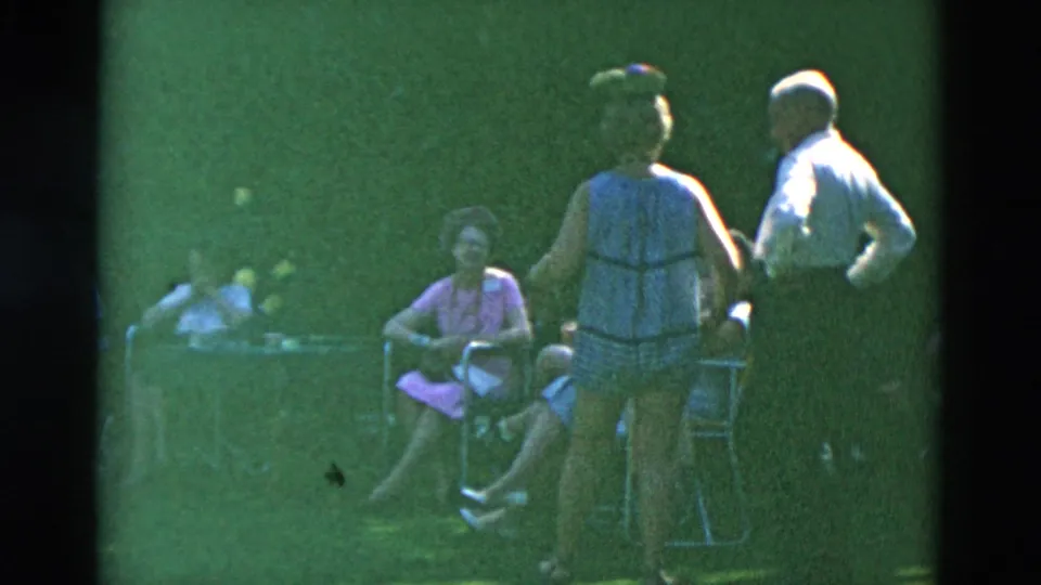 1958 Oregon backyard scene with a sleeveless-dressed woman and shirted man standing beside seated adults on folding chairs.