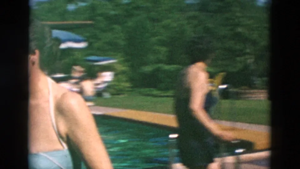 A handheld 8mm frame shows adults in swimsuits moving quickly near a backyard pool, with motion blur and green lawn visible.