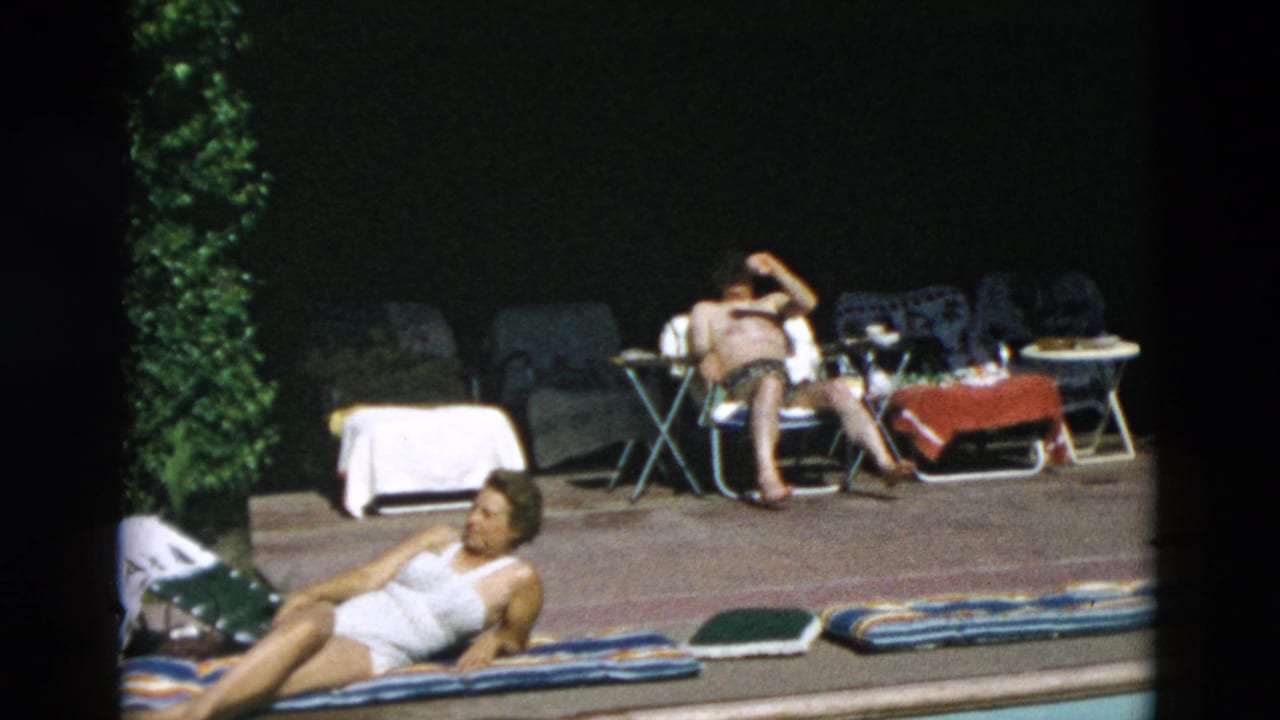 Adults relaxing beside a pool with towels, lounge chairs, and small tables.