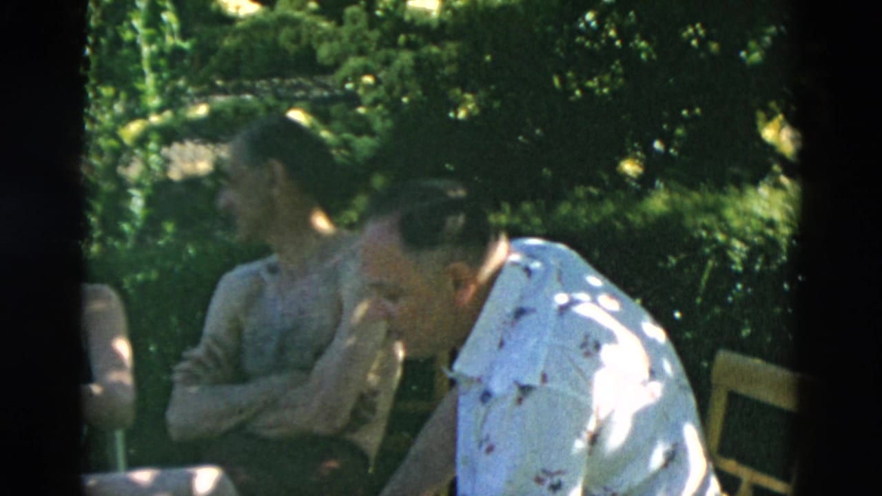 Adults seated outdoors at a shaded picnic table with trees behind them.
