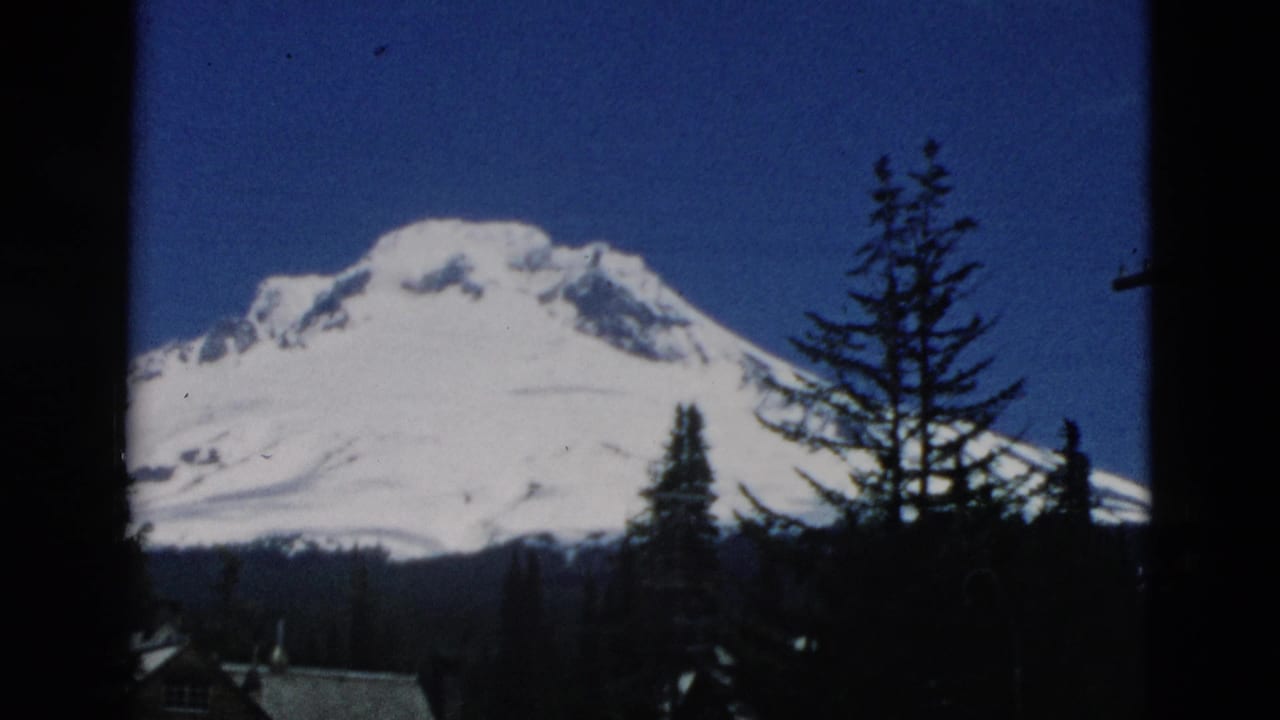 Snowy mountain peak behind evergreen trees, framed by dark film edges.