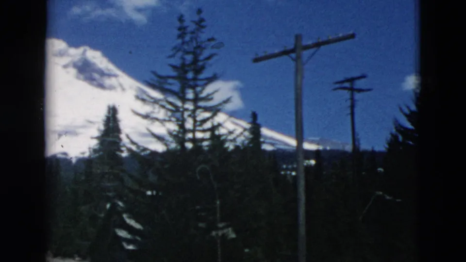 1958 8mm frame during a pan, showing the mountain partly obscured by evergreens and utility poles.