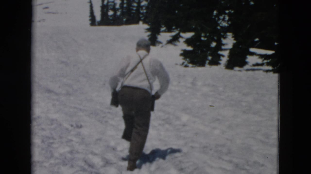 Man continues uphill through snow with trees at the edge of the slope.
